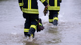 Feuerwehrleute gehen über eine überflutet Straße in Dasing im schwäbischen Landkreis Aichach-Friedberg. Nach einer erfolgreichen Testphase soll die Ehrenamtskarte in Baden-Württemberg 2025 im ganzen Land eingeführt werden.