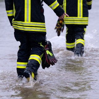 Feuerwehrleute gehen über eine überflutet Straße in Dasing im schwäbischen Landkreis Aichach-Friedberg. Nach einer erfolgreichen Testphase soll die Ehrenamtskarte in Baden-Württemberg 2025 im ganzen Land eingeführt werden.