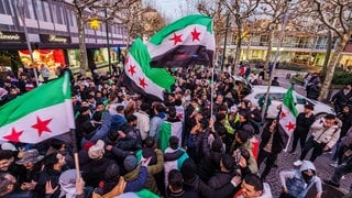 Exil-Syrer feiern den Sturz des Assad-Regime und schwenken dabei die syrische Nationalflagge.