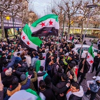 Exil-Syrer feiern den Sturz des Assad-Regime und schwenken dabei die syrische Nationalflagge.