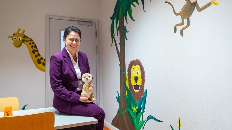 Marion Gentges (CDU), Justizministerin von Baden-Württemberg, sitzt in der Justizvollzugsanstalt Mannheim im neu gestalteten Kinderbesuchsraum und hält dabei das neue JVA-Maskottchen "Toni" in ihren Händen.