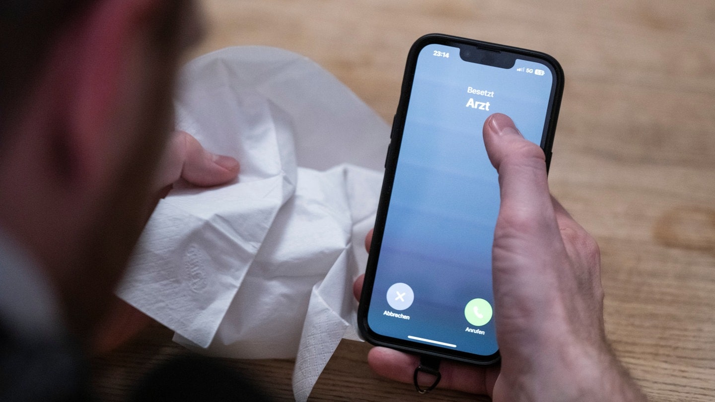 Ein Mann hält ein Taschentuch in einer Hand und ein Telefon mit dem Schriftzug 