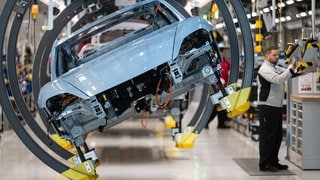 Ein Mitarbeiter der Porsche AG montiert in einer Produktionshalle des Porsche-Stammwerks einen Porsche Taycan. Auch bei Porsche schwächelt das Geschäft. Medien berichten von 8.000 Jobs, die auf der Kippe stehen. Ein Branchenexperte gibt Entwarnung.