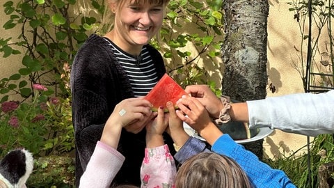 Lucie bekommt von allen Kindern eine Wassermelone gereicht