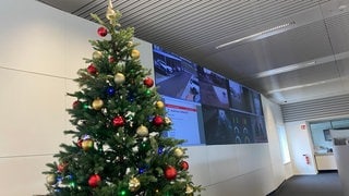 Ein Weihnachtsbaum steht in einem Büro vor mehreren Bildschirmen.