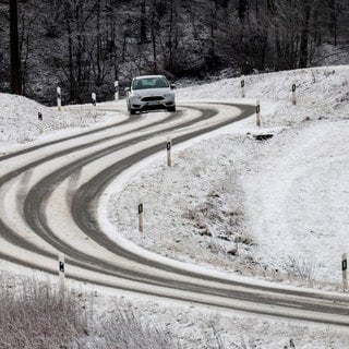 Ein Auto ist bei winterlichen Straßenverhältnissen auf der Schwäbischen Alb unterwegs.