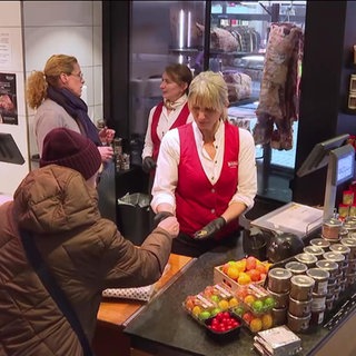 Eine ältere Frau steht an einer Ladentheke und bezahlt