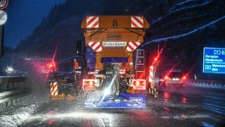 Ein Fahrzeug vom Winterdienst streut Streumittel bei Schneefall auf einer glatten Straße.