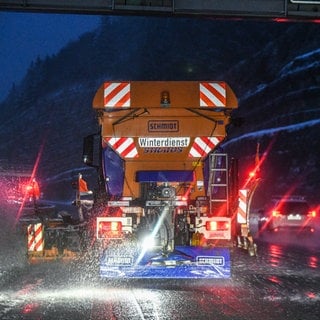 Ein Fahrzeug vom Winterdienst streut Streumittel bei Schneefall auf einer glatten Straße.