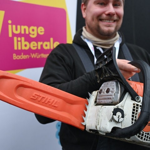 Mark Hohensee, Landesvorsitzender der Jungen Liberalen, der Jugendorganisation der FDP, hält vor dem Eingang der Schwabenlandhalle vor dem Beginn des Landesparteitags der BW-FDP eine Motorsäge in der Hand. Er will damit für einen Bürokratieabbau mit der Kettensäge demonstrieren.