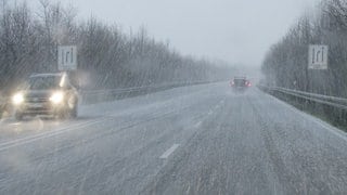 Autos fahren während eines Gewitters mit Graupel auf einer mit Graupelkörnern bedeckten Straße.