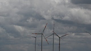 Windräder drehen sich vor dichten grauen Regenwolken nahe Scharenstetten in Baden-Württemberg.