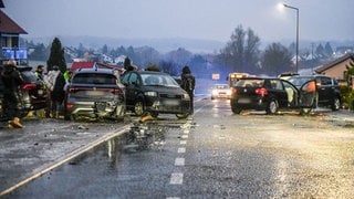 Nach einem Unfall bei Glatteis mit mehreren Fahrzeugen stehen Helfer und Beteiligte an den Autos auf einer Straße in Aalen. Auf spiegelglatten Straßen hat die Polizei in Baden-Württemberg am Mittwoch insgesamt weit mehr als 100 Unfälle gezählt.