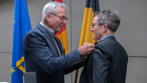 Innenminister Thomas Strobl (CDU, l) befestigt bei der Verleihung der Rettungsmedaille im Innenministerium die Rettungsmedaille an dem Anzug von Tobias Schneller, einem 53-jährigen Lehrer. Tobias Schneller hatte im April 2024 nach einer Messerattacke auf ein vierjähriges Mädchen in einem Supermarkt in Wangen im Allgäu den Täter entwaffnet, verfolgt und die Polizei alarmiert.