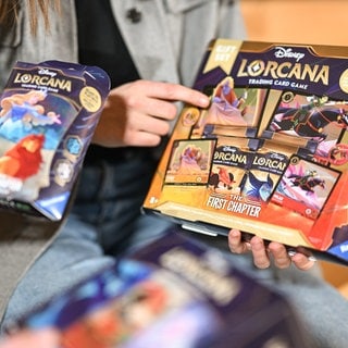 Zwei Mitarbeiterinnen des Spieleherstellers Ravensburger AG halten das neue Sammelkartenspiel Disney Lorcana Trading Card Game, The First Chapter in den Händen. Das Sammelkartenspiel wird von der Ravensburger AG hergestellt und beschert dem Unternehmen Umsätze in Millionen-Höhe.