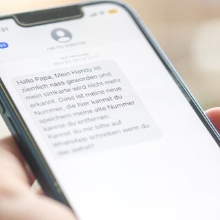 Eine Frau hält ein Smartphone in ihrer Hand, auf dessen Display eine Betrugs-SMS zu lesen ist. 
