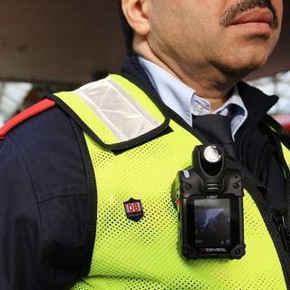 An der Weste eines Sicherheitsmitarbeiters der Deutschen Bahn hängt eine Bodycam.