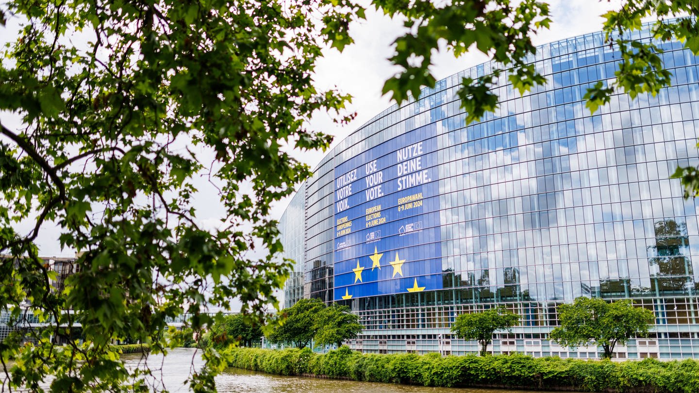 Der Himmel spiegelt sich in der gläsernen Fassade des Europäischen Parlaments in Straßburg. Ein großes Banner wirbt für die Europawahl.