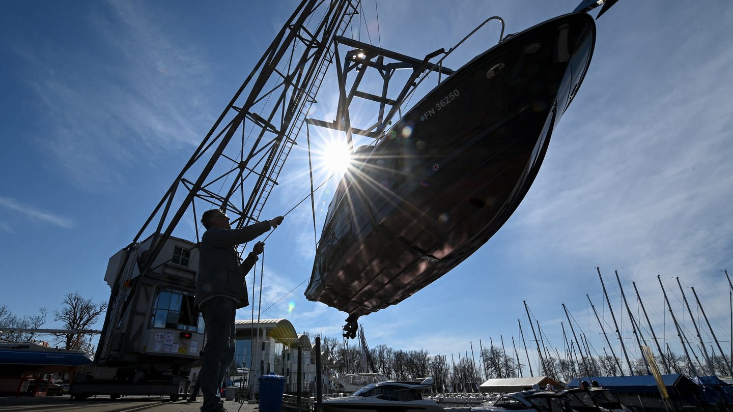 Ein Kran hievt eine kleine Yacht in den Yachthafen am Bodensee