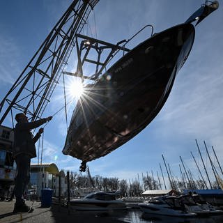 Ein Kran hievt eine kleine Yacht in den Yachthafen am Bodensee