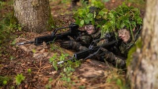 Soldaten der Bundeswehr mit Tarnzweigen auf dem Kopf bei einer Übung im Wald.
