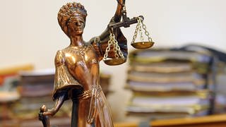 Justizia-Figur vor Aktenstapeln