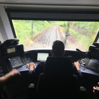 Ein Lokführer sitzt im Zug-Cockpit und steuert den Zug über die Schienen.
