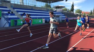 Sportlerinnen und Sportler laufen auf Bahn auf einem Sportplatz