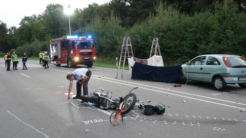 Ein Polizist sprüht Markierungen für die Aufnahme des Unfallhergangs rund um ein Motorrad, das nach einem Unfall auf der Straße liegt.
