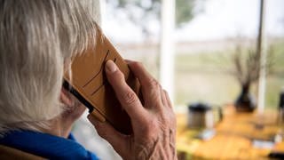 Eine Seniorin hält ein Telefon ans Ohr.