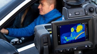 Mann mit Anschnallgurt in einem Auto, Monitor zeigt Wärmebild