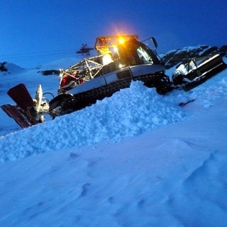 Eine Pistenraupe im Abendlicht auf einem Berghang. Eine Pistenraupe wie diese hat zwei Skifahrer am Arlberg überfahren.