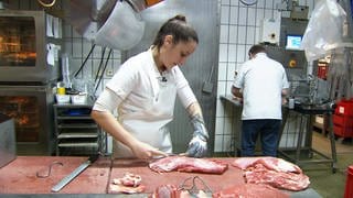 Eine Metzgerin zerteilt ein Stück Fleisch auf einer Arbeitsfläche