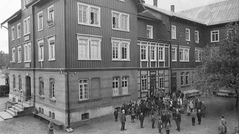 Vor einem großen Haus in Wilhelmsdorf stehen viele Menschen. Das Foto ist schwarz-weiß.