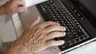 Die Hand eines älteres Mannes tippt auf der Tastatur eines Laptops. 