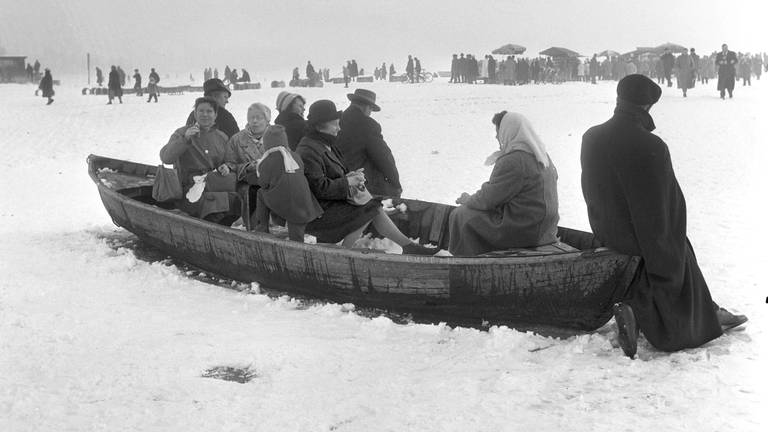 Auf dem Bild sieht man in einem eingefrorenen Fischerboot wartende Zuschauer in der Nähe von Hagnau 