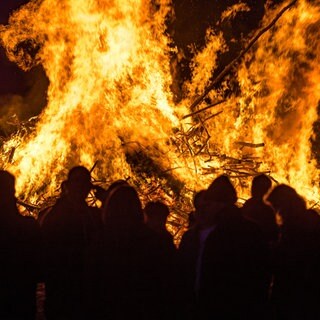 Menschen stehen vor einem brennenden Osterfeuer.