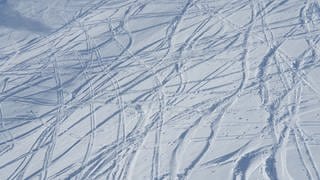 Eine Skipiste, auf der die ersten Skifahrer ihre Spuren in den Schnee gezogen haben.