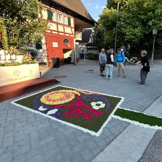 Ein bunter Blumenteppich liegt auf der Straße und führt zu einem Altar.