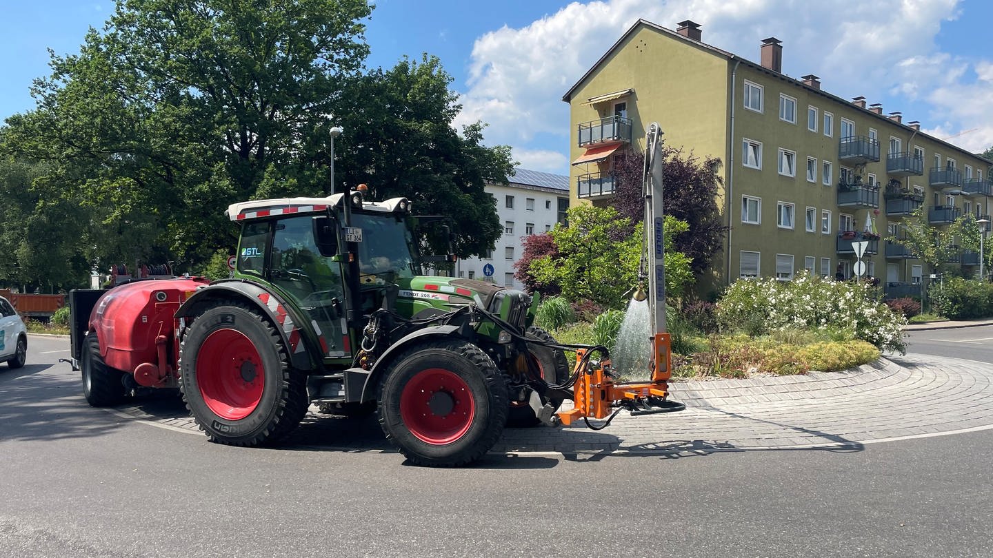 Ein Einsatzfahrzeug der Garten- und Tiefbaubetriebe Lindau gießt Wasser auf Büsche am Straßenrand