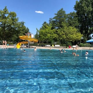 In einem Freibad schwimmen Badegäste, im Hintergrund ist eine Wasserrutsche zu sehen.