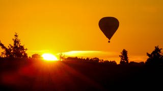 Heißluftballon fährt am Himmel, während die Sonne aufgeht (Symbolfoto).