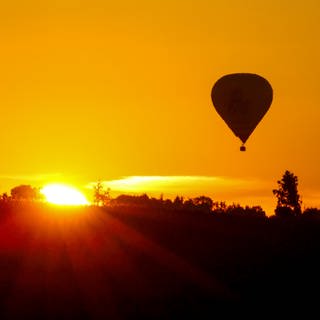 Heißluftballon fährt am Himmel, während die Sonne aufgeht (Symbolfoto).