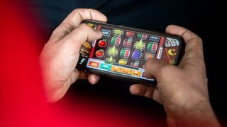 Ein Mann spielt am Handy ein Spiel eines Online-Casinos. 