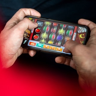 Ein Mann spielt am Handy ein Spiel eines Online-Casinos. 