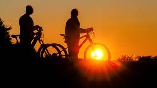 Zwei Radfahrerinnen schauen sich am Morgen den Sonnenaufgang an.