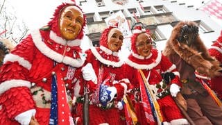 Personen in Narrenhäs und mit Maske schunkeln miteinander.