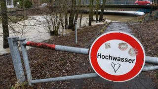 Ein Schild mit der Aufschrift Hochwasser steht am Ufer des Flusses Rotach. Die Rotach tritt kurz vor der Mündung in den Bodensee über die Ufer.