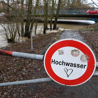 Ein Schild mit der Aufschrift Hochwasser steht am Ufer des Flusses Rotach. Die Rotach tritt kurz vor der Mündung in den Bodensee über die Ufer.