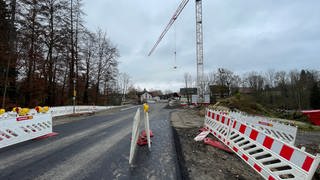 Absperrungen und ein Kran stehen auf der Baustelle für eine Brücke. 